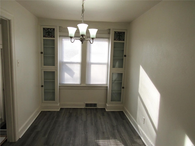 unfurnished dining area with dark wood-type flooring and an inviting chandelier