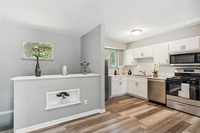 kitchen with light hardwood / wood-style flooring, a wealth of natural light, tasteful backsplash, white cabinetry, and stainless steel appliances