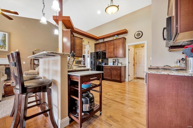 kitchen with light hardwood / wood-style floors, black appliances, hanging light fixtures, light stone countertops, and a breakfast bar area