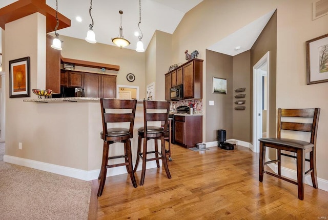 kitchen with light stone countertops, decorative light fixtures, stainless steel stove, kitchen peninsula, and light wood-type flooring