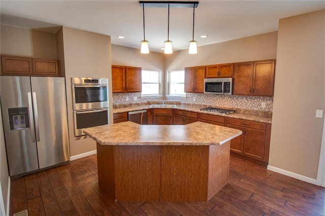 kitchen featuring appliances with stainless steel finishes, brown cabinets, decorative light fixtures, and a kitchen island