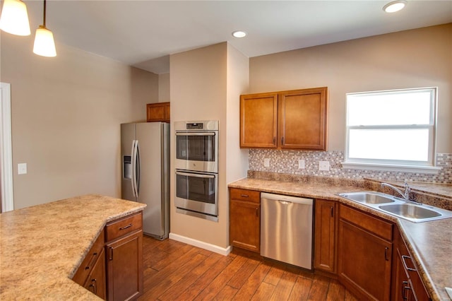 kitchen featuring dark wood finished floors, hanging light fixtures, backsplash, appliances with stainless steel finishes, and a sink