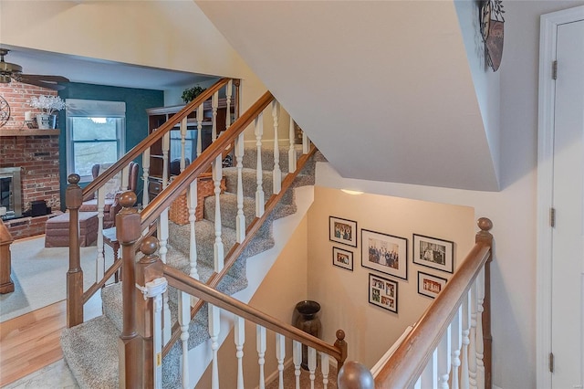 stairs with hardwood / wood-style floors, vaulted ceiling, and a brick fireplace