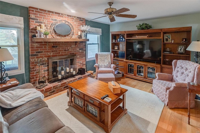 living room featuring a wealth of natural light, light hardwood / wood-style flooring, ceiling fan, and a brick fireplace