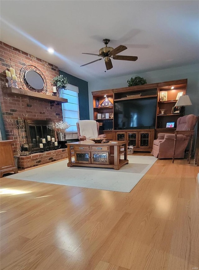 living room featuring a brick fireplace, ceiling fan, and light hardwood / wood-style flooring