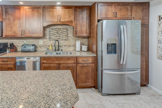 kitchen with backsplash, light stone countertops, sink, and appliances with stainless steel finishes