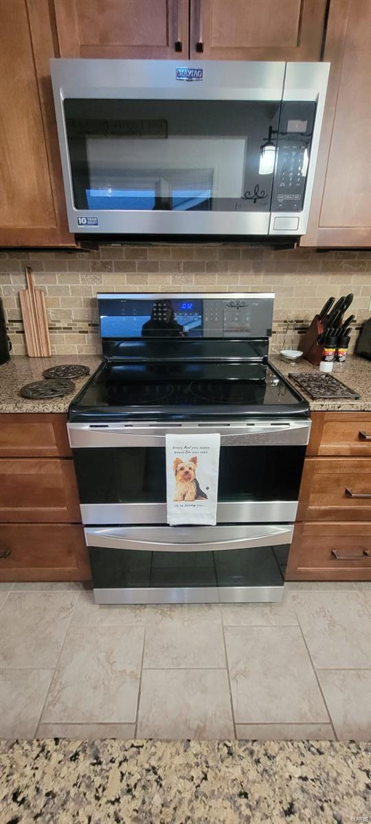 kitchen featuring light tile patterned flooring, light stone countertops, stainless steel appliances, and tasteful backsplash