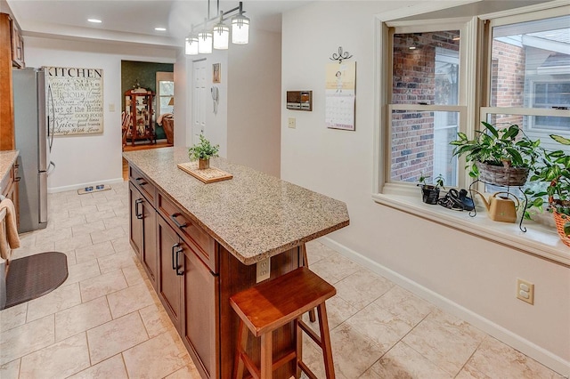 kitchen with stainless steel refrigerator, a center island, light stone counters, pendant lighting, and a kitchen bar