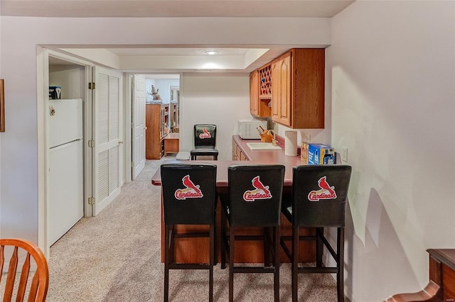 kitchen with sink, a kitchen breakfast bar, kitchen peninsula, white appliances, and light carpet