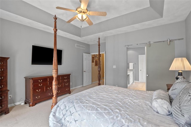 carpeted bedroom featuring a barn door, a raised ceiling, and ceiling fan