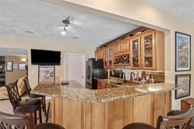 kitchen featuring a kitchen breakfast bar, black fridge, sink, light stone countertops, and kitchen peninsula