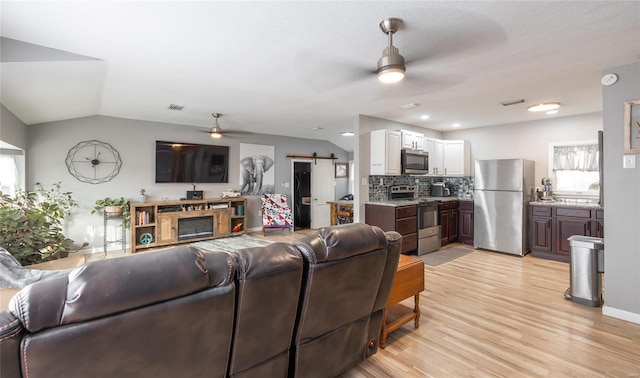 living room featuring a barn door, ceiling fan, vaulted ceiling, and light wood-type flooring