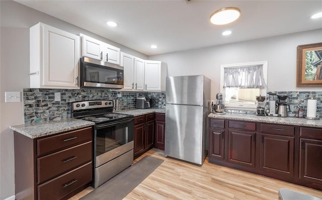 kitchen with decorative backsplash, appliances with stainless steel finishes, light stone counters, light hardwood / wood-style floors, and white cabinetry