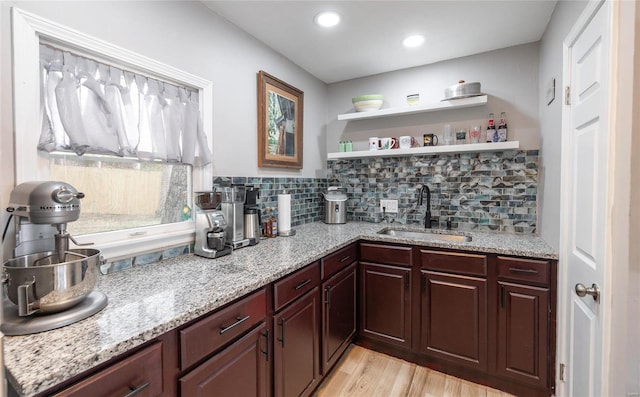 bar with tasteful backsplash, light stone counters, dark brown cabinets, sink, and light hardwood / wood-style floors