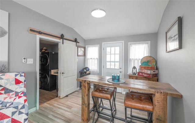 dining room featuring a barn door, stacked washer / drying machine, lofted ceiling, and light hardwood / wood-style flooring