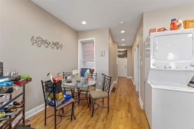 clothes washing area with light hardwood / wood-style flooring and stacked washer / drying machine