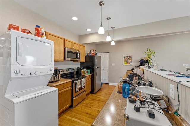 kitchen with appliances with stainless steel finishes, light wood-type flooring, hanging light fixtures, and stacked washer and clothes dryer