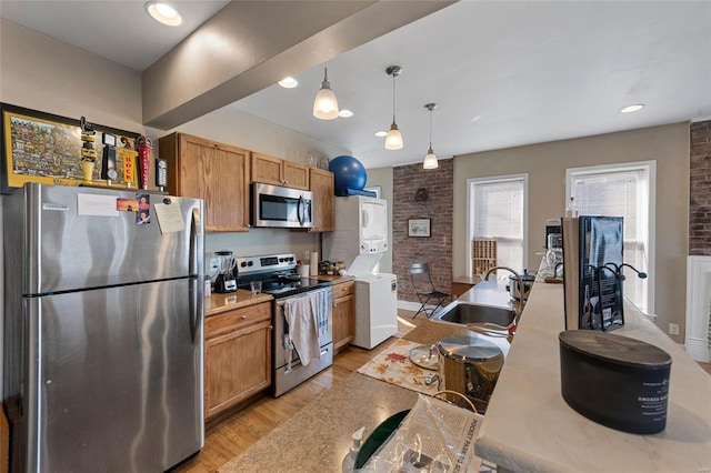 kitchen with pendant lighting, sink, stacked washer and dryer, light hardwood / wood-style floors, and stainless steel appliances