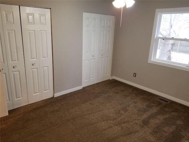 unfurnished bedroom with dark carpet and two closets