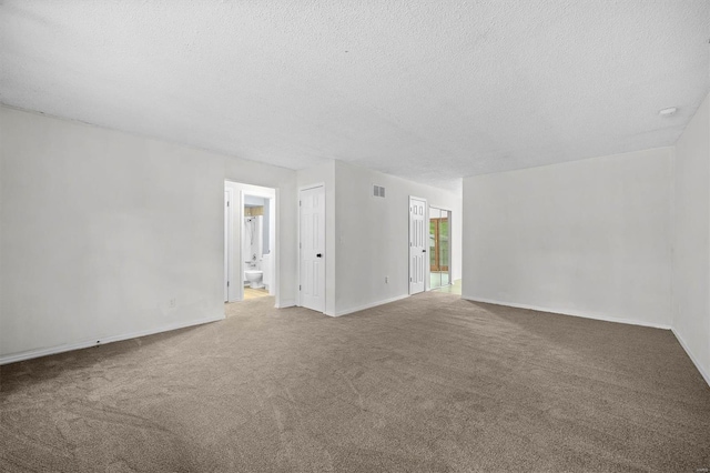 empty room with carpet floors, baseboards, a textured ceiling, and visible vents