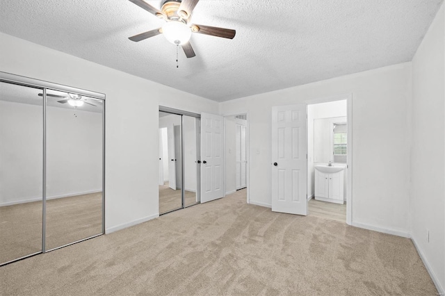 unfurnished bedroom with a textured ceiling, multiple closets, carpet, and ensuite bath