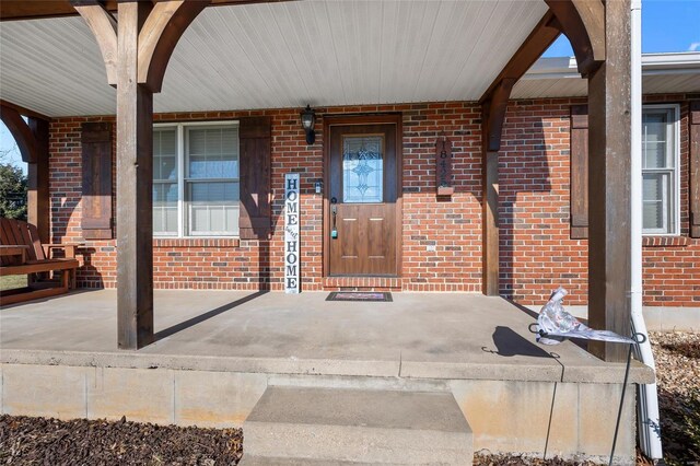 view of exterior entry featuring covered porch and brick siding