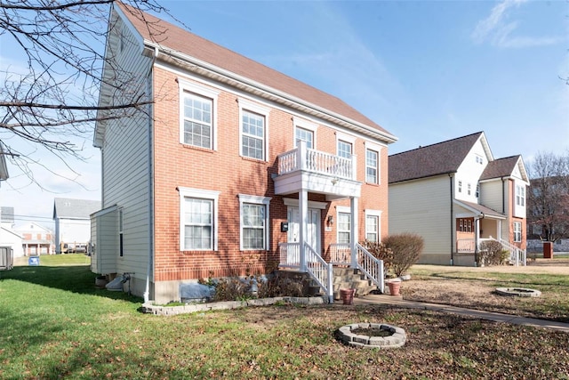 view of front of property with a balcony, a front yard, and an outdoor fire pit