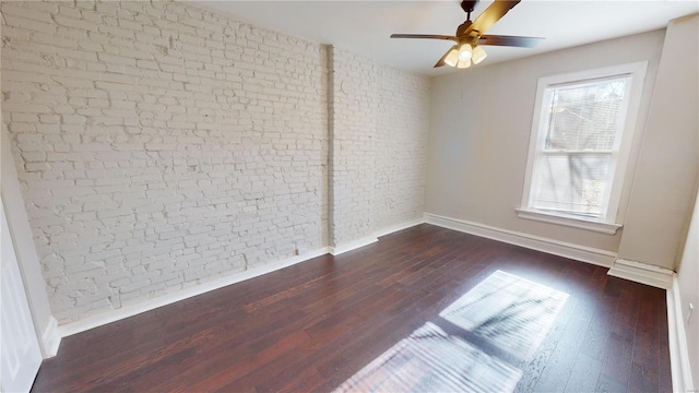 empty room with a wealth of natural light, ceiling fan, dark wood-type flooring, and brick wall