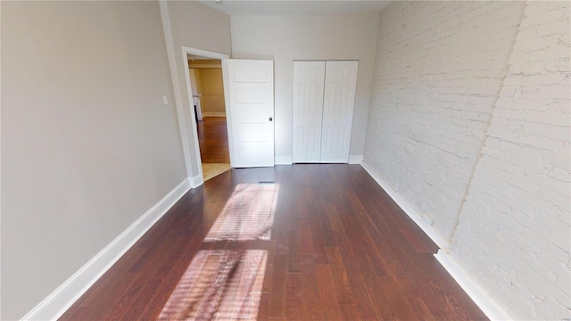 hallway featuring dark wood-type flooring and brick wall