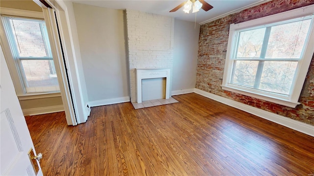 unfurnished living room with hardwood / wood-style flooring, plenty of natural light, a fireplace, and brick wall