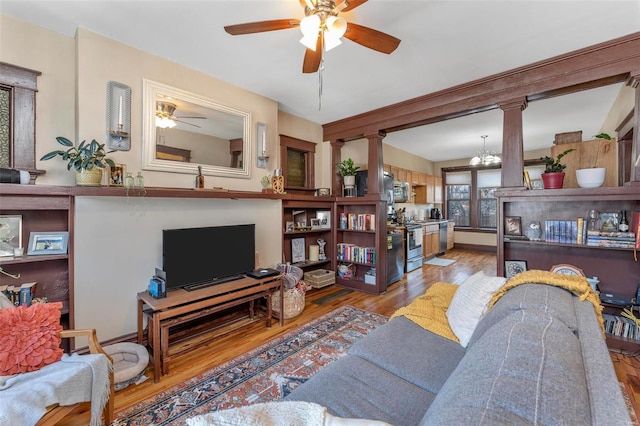 living room with wood-type flooring, ceiling fan with notable chandelier, and decorative columns