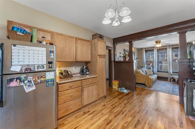 kitchen featuring stainless steel fridge, ornate columns, ceiling fan with notable chandelier, decorative light fixtures, and light hardwood / wood-style floors