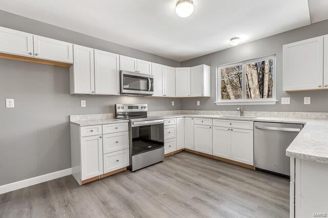 kitchen featuring stainless steel appliances, light hardwood / wood-style floors, white cabinetry, and sink