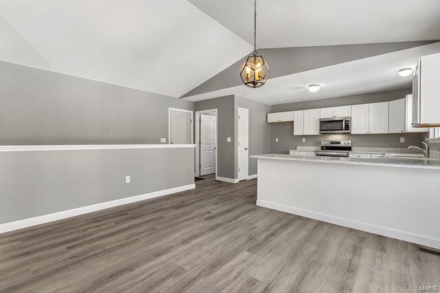 kitchen with white cabinetry, stainless steel appliances, hanging light fixtures, vaulted ceiling, and sink