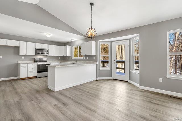 kitchen with vaulted ceiling, stainless steel appliances, white cabinetry, and decorative light fixtures