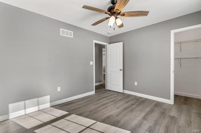 unfurnished bedroom with ceiling fan, a closet, a spacious closet, and light wood-type flooring