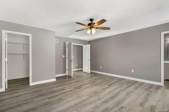 unfurnished bedroom featuring ceiling fan, a walk in closet, a closet, and hardwood / wood-style floors