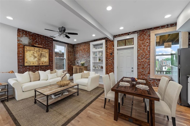 living room featuring beam ceiling, ceiling fan, brick wall, and light hardwood / wood-style floors