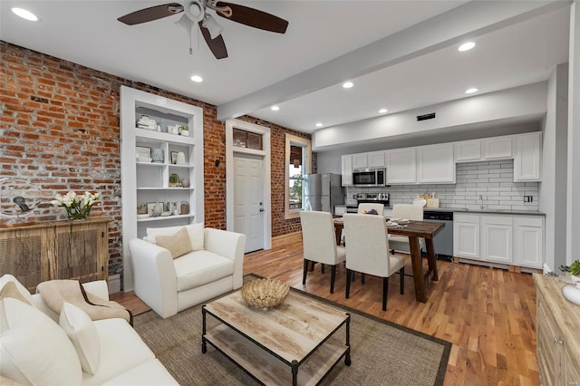 living room featuring ceiling fan, light hardwood / wood-style flooring, brick wall, and sink