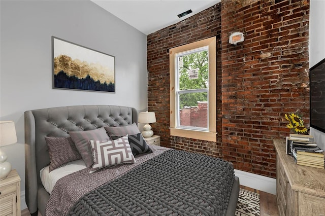 bedroom with hardwood / wood-style floors and brick wall