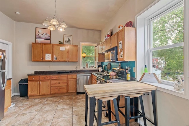 kitchen featuring hanging light fixtures, a notable chandelier, light tile patterned flooring, a kitchen bar, and stainless steel appliances