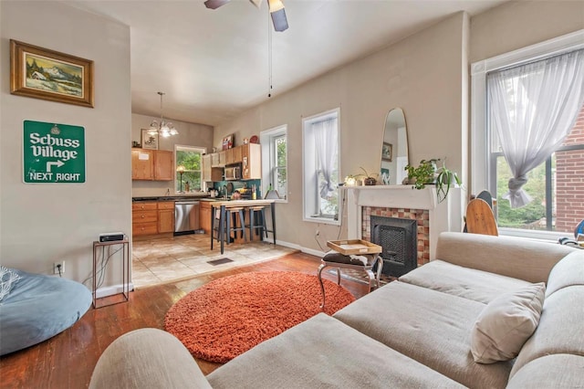 living room with lofted ceiling, light wood-type flooring, ceiling fan with notable chandelier, and a brick fireplace