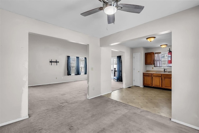 unfurnished living room with ceiling fan, sink, plenty of natural light, and light carpet