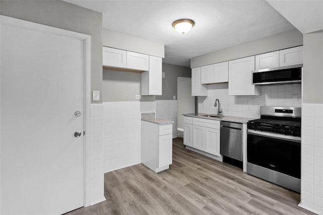 kitchen with sink, stainless steel appliances, light stone counters, light hardwood / wood-style flooring, and white cabinets