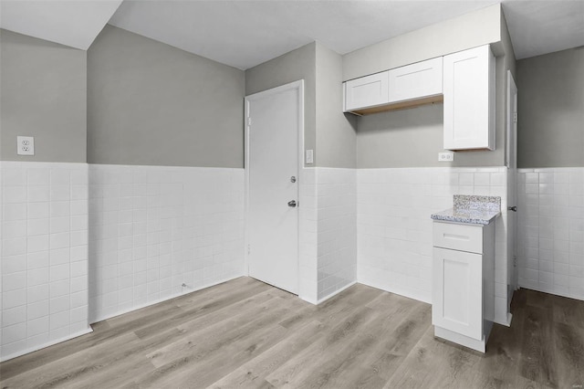 kitchen featuring white cabinets, light wood-type flooring, and tile walls