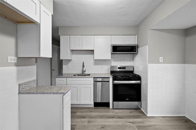 kitchen featuring sink, light stone counters, light hardwood / wood-style floors, white cabinets, and appliances with stainless steel finishes