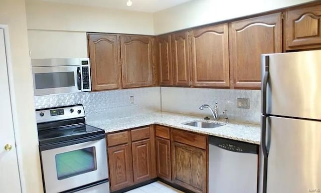 kitchen featuring tasteful backsplash, light stone counters, sink, and appliances with stainless steel finishes