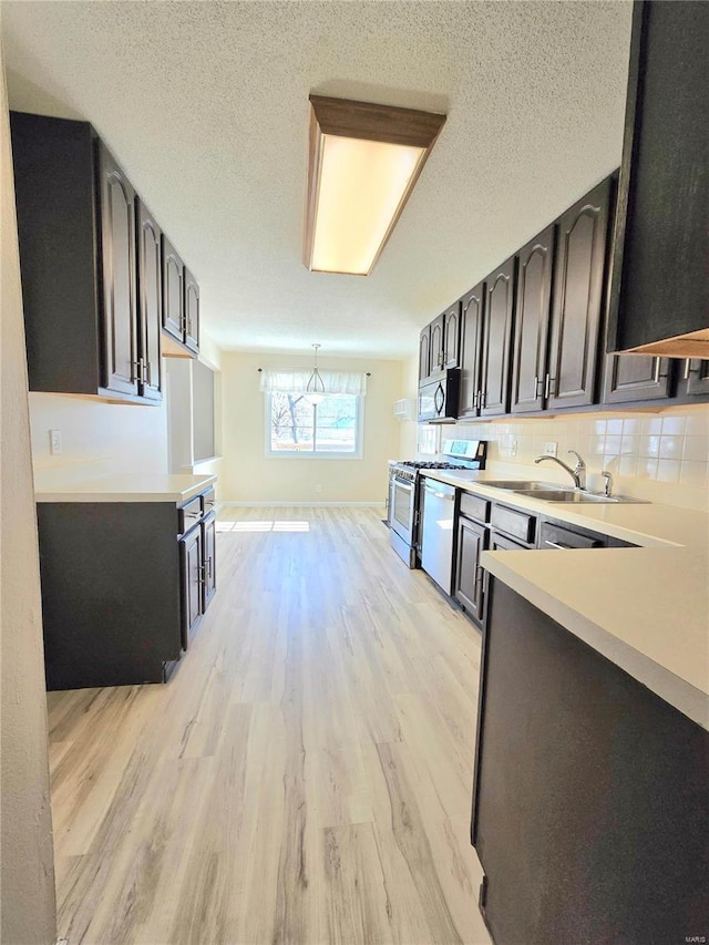 kitchen with sink, dishwashing machine, backsplash, light hardwood / wood-style floors, and gas stove