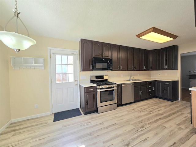 kitchen featuring dark brown cabinetry, sink, hanging light fixtures, light wood-type flooring, and stainless steel appliances