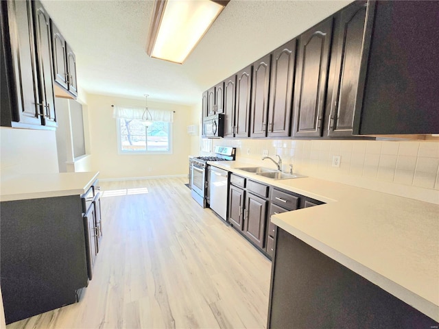 kitchen featuring appliances with stainless steel finishes, decorative light fixtures, tasteful backsplash, sink, and light hardwood / wood-style floors